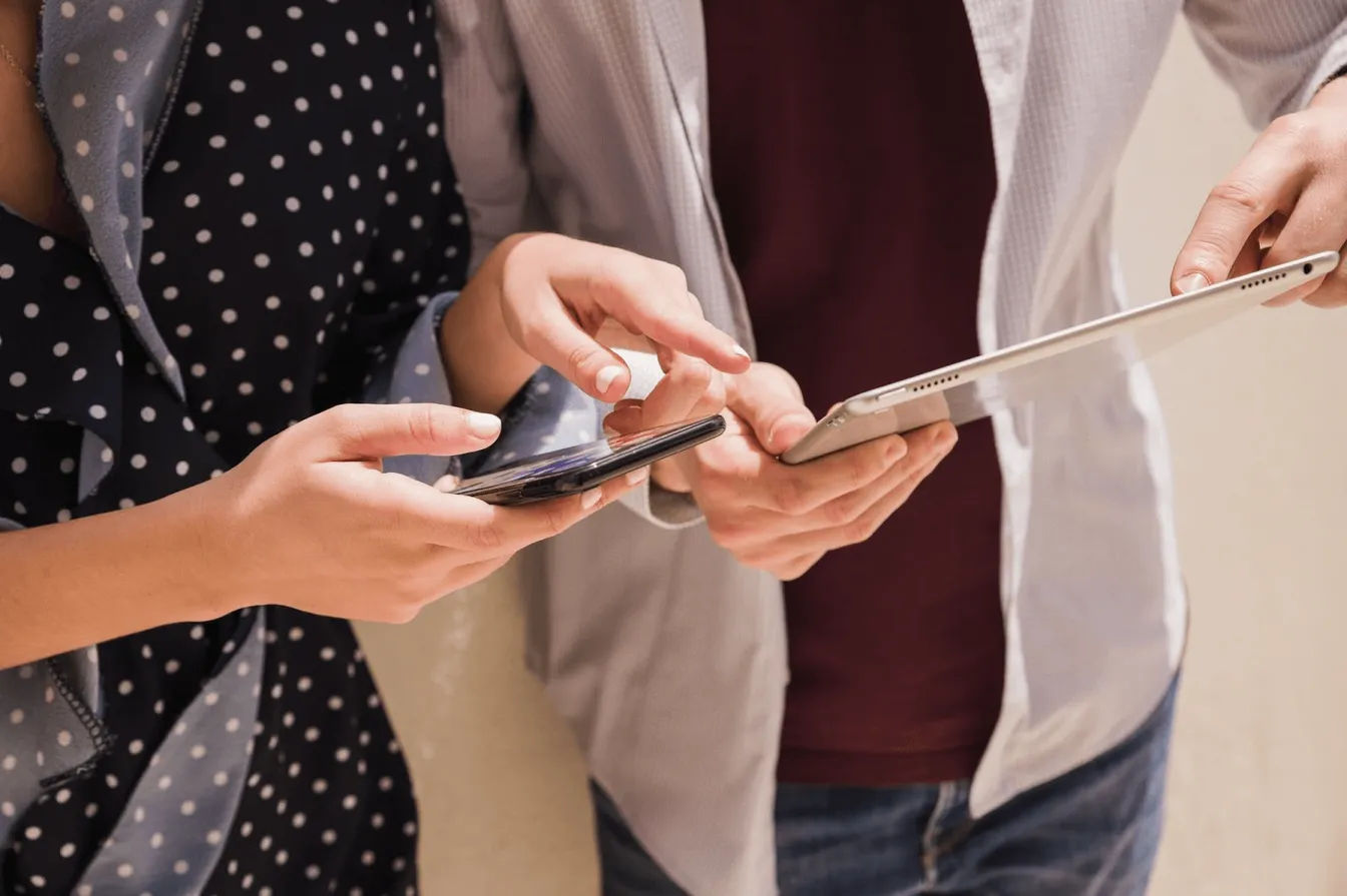 Two person holding a phone and a tablet